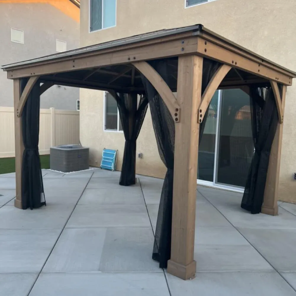 Wood gazebo with hardtop metal roof and netting assembled on a backyard concrete patio