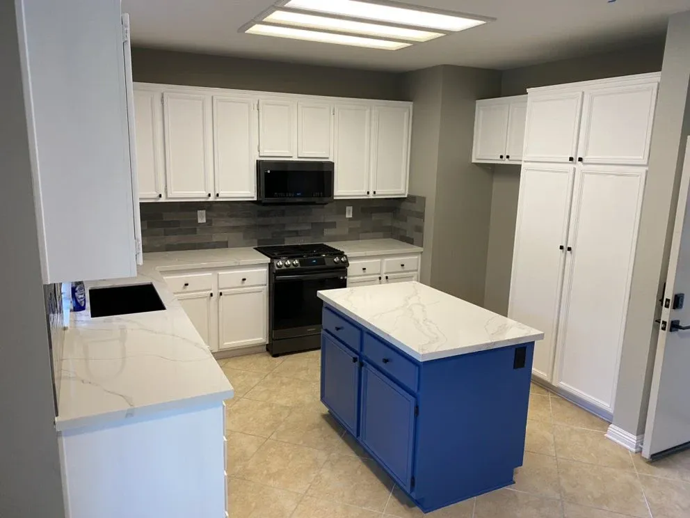 Refreshed kitchen with white refinished cabinets, blue-painted island, quartz countertops, and slate tile backsplash