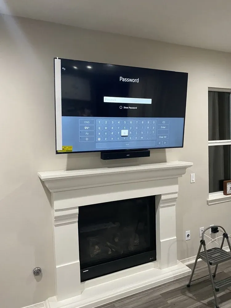 Large TV and soundbar mounted level above a white fireplace mantel